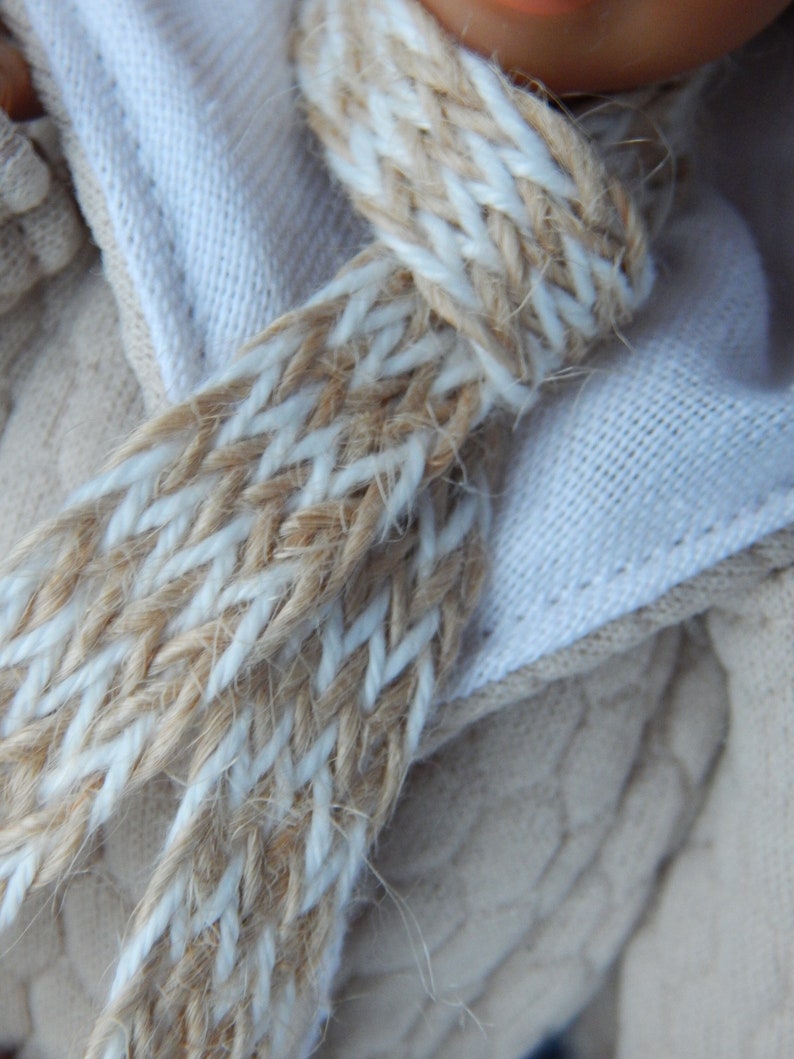 Puede incluir: Primer plano de una bufanda de punto beige y blanca. La bufanda est&aacute; hecha de un hilo grueso y texturizado y tiene un patr&oacute;n de espiga.