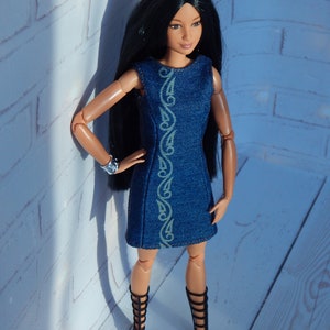 May include: A fashion doll with long black hair wearing a blue denim dress with a white design and black gladiator sandals.