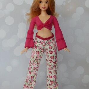 May include: A doll wearing a pink crop top with a bow and white pants with a floral pattern.