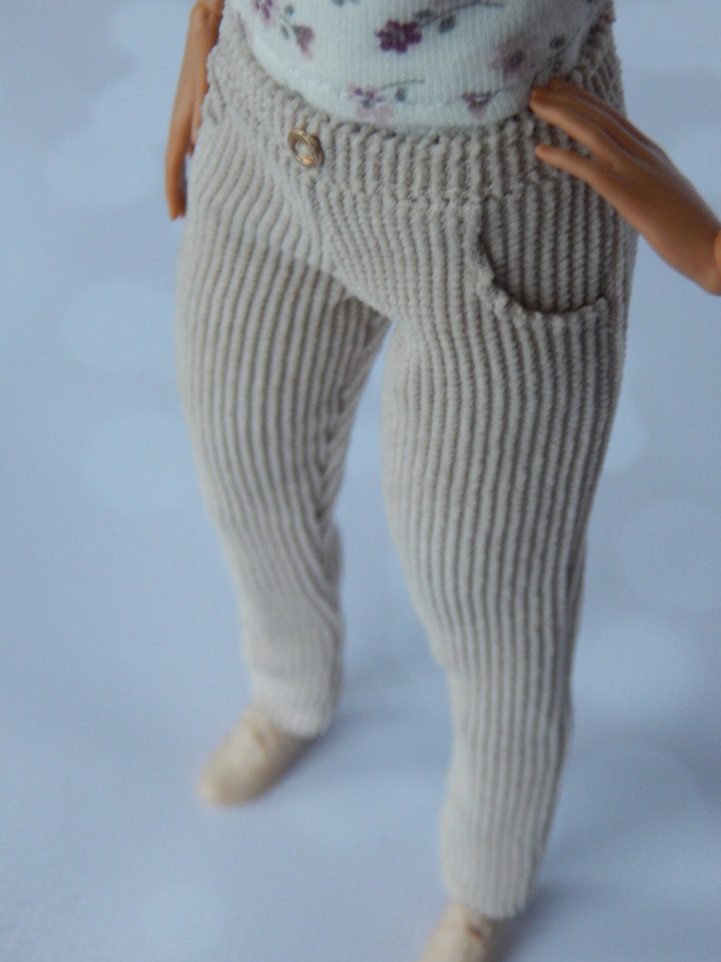 May include: Beige corduroy pants with a button and a pocket. The pants are made of a soft, textured fabric.