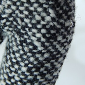 May include: Close-up of black and white tweed fabric with a small silver button.