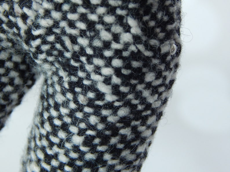 May include: Close-up of black and white tweed fabric with a small silver button.