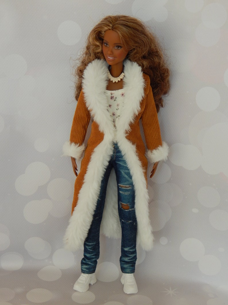 May include: A doll wearing a brown corduroy coat with a white faux fur trim, blue jeans with a distressed detail, and white sneakers. The doll has long brown hair and brown eyes.