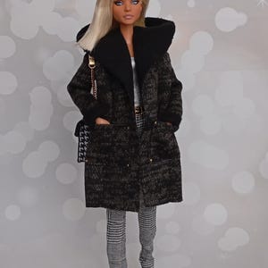 May include: A doll wearing a long, dark green and black patterned coat with a black collar and pockets. The doll is also wearing black and white checkered pants, black and white shoes, and carrying a black and white purse with a gold chain.