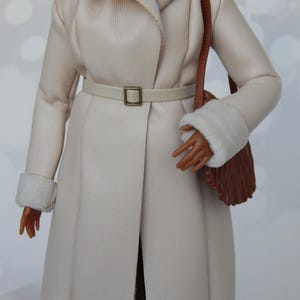 May include: A white faux fur coat with a brown leather strap and a brown fringe bag. The coat has a white fur collar and cuffs. The coat is belted with a white leather belt with a gold buckle.
