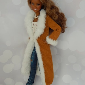 May include: A doll wearing a brown corduroy coat with a white fur trim, blue jeans, and white sneakers. The doll has brown hair and brown eyes.