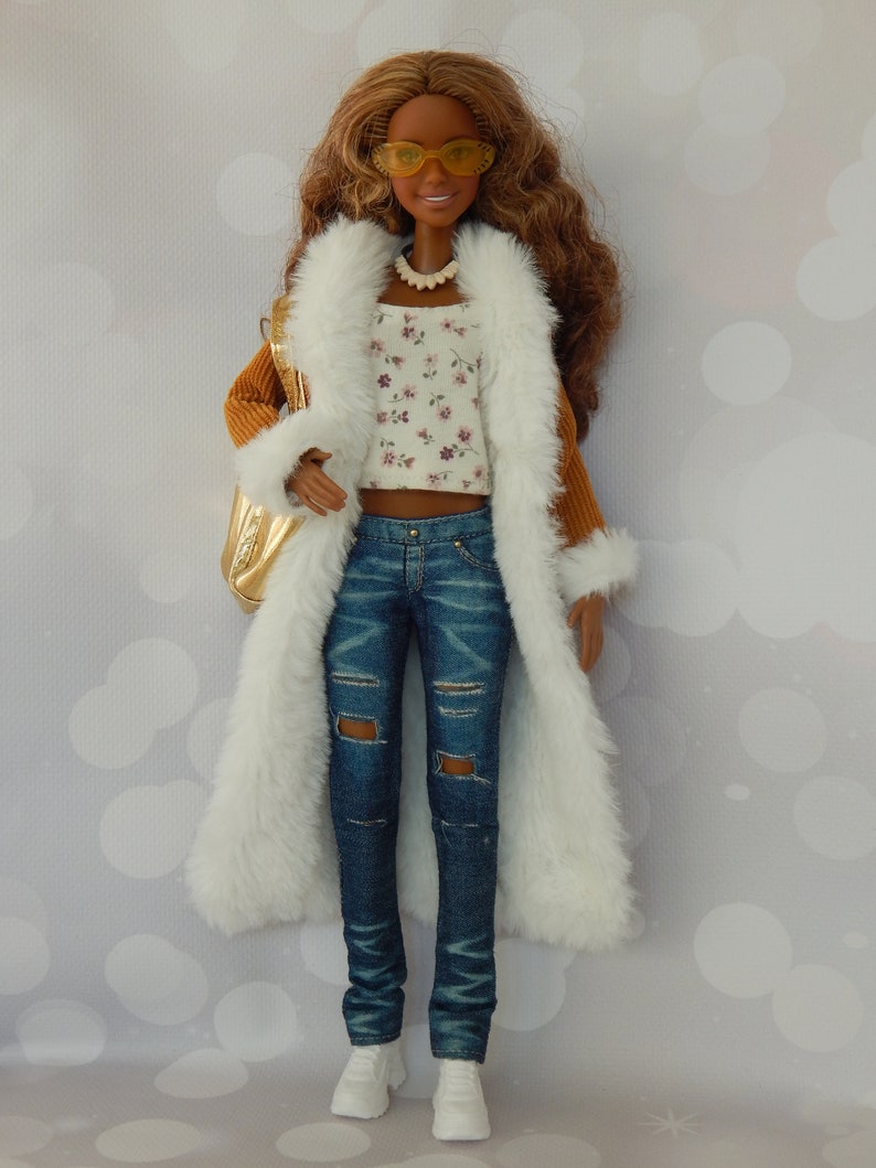 May include: A doll with brown hair wearing a white faux fur coat, a brown corduroy jacket, a white floral top, blue jeans with rips, and white sneakers. The doll is wearing yellow sunglasses and a brown beaded necklace.