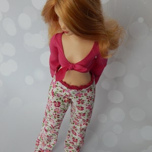 May include: A doll wearing a pink crop top with a bow and floral print pants.