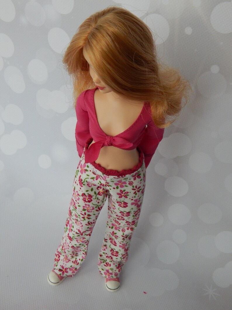 May include: A doll wearing a pink crop top with a bow and floral print pants.