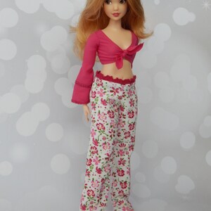 May include: A doll with long, wavy, light brown hair wearing a pink crop top with a tie at the front and white pants with a pink floral pattern.