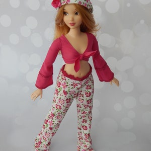 May include: A doll wearing a pink and white floral print outfit. The doll has long red hair and is wearing a white hat with pink flowers. The doll is wearing a pink crop top with a white floral print pants. The doll is wearing white sneakers.