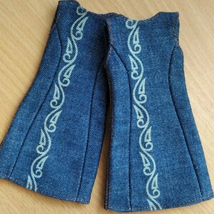 May include: A pair of denim overalls with a white embroidered design. The overalls have a wide leg and a sleeveless design.