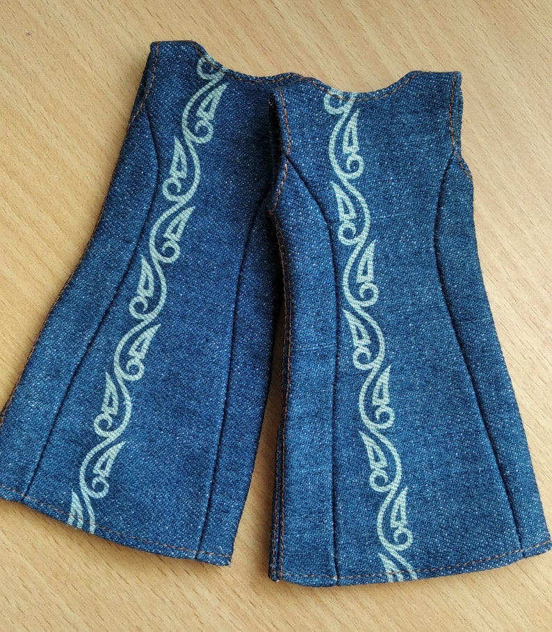 May include: A pair of denim overalls with a white embroidered design. The overalls have a wide leg and a sleeveless design.