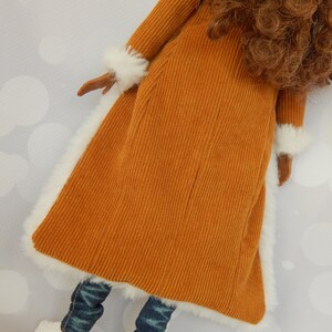 May include: A brown corduroy coat with white fur trim. The coat is worn over blue jeans and white shoes.