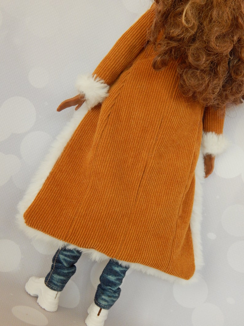 May include: A brown corduroy coat with white fur trim. The coat is worn over blue jeans and white shoes.