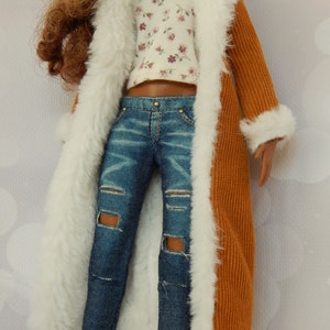 May include: A doll wearing a brown corduroy coat with a white fur trim, a white floral print top, and blue jeans with distressed details.