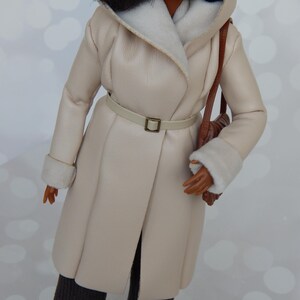 May include: A cream-colored faux fur coat with a brown leather belt and a brown leather handbag. The coat has a white faux fur lining around the collar and cuffs.