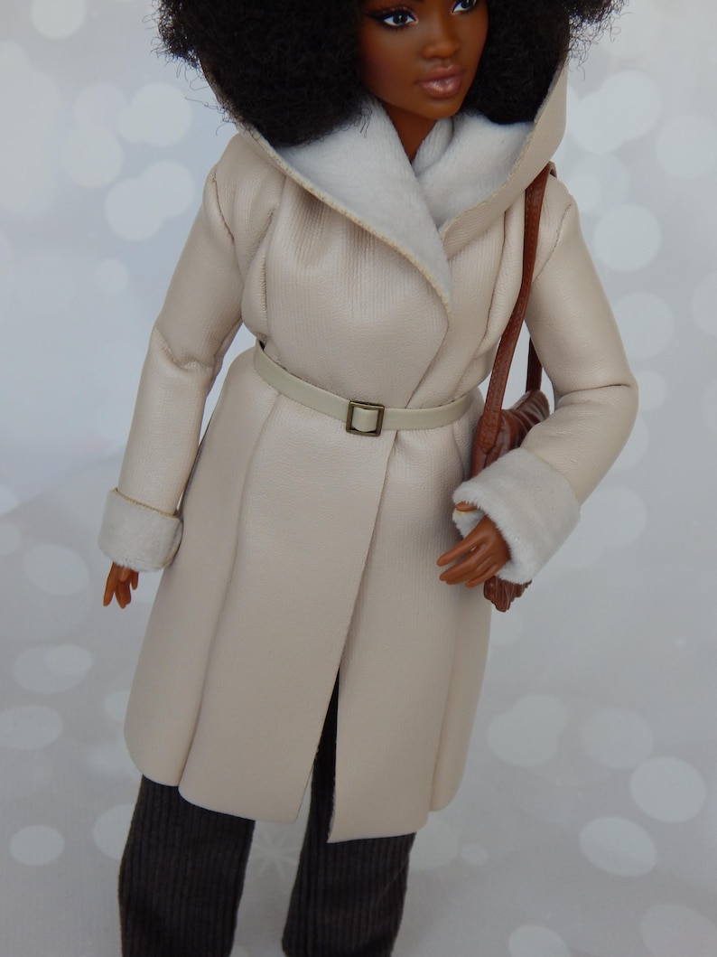 May include: A cream-colored faux fur coat with a brown leather belt and a brown leather handbag. The coat has a white faux fur lining around the collar and cuffs.