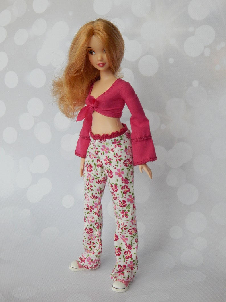 May include: A doll with long, wavy, red hair wearing a pink crop top with a bow and white pants with a floral pattern.