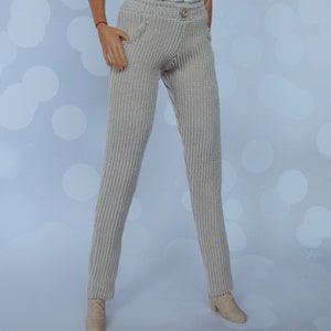 May include: A pair of beige corduroy pants with a button closure and a pocket on the front. The pants are on a doll.
