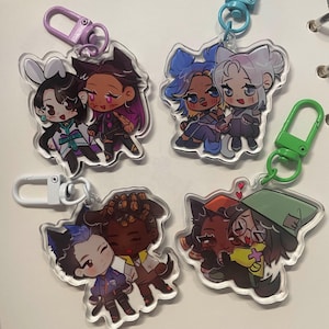 May include: Four clear acrylic keyrings featuring cartoon couples. Each keyring has a different couple design with vibrant colours and attached metal clasps in various colours. The couples are hugging or standing close together.