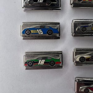 以下が含まれることがあります： レースカーのチャームが付いたシルバーのチャームブレスレット2本。チャームは青と緑で、黒と白のディテールが施されています。車には15と18の数字が書かれています。