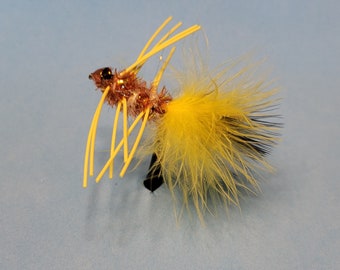May include: A detailed close-up of a fishing fly. The fly features a brown body with yellow and black feathers, and yellow antennae. The fly is designed to mimic an insect and is used to attract fish.