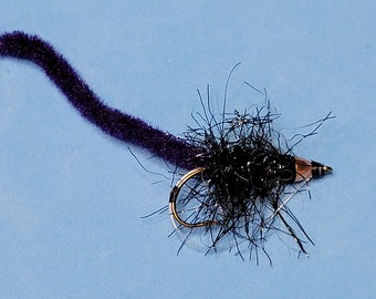 May include: A fishing fly with a dark purple body and a black, fluffy head. The fly has a gold hook and a tail with orange, yellow, and pink strands. The fly is designed for catching fish.