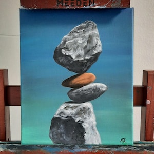 Könnte beinhalten: Acrylbild auf Leinwand, das einen Stapel ausbalancierter Steine vor einem blau-grünen Farbverlaufshintergrund zeigt. Die Steine sind in Grau- und Brauntönen gehalten, mit den Initialen des Künstlers unten rechts. Das Wort "MEEDEN" steht oben.