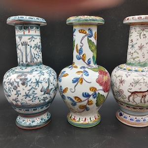 Peut inclure: Trois vases en céramique avec des motifs floraux et animaliers peints à la main. Les vases sont blancs avec des accents bleus, verts, jaunes et rouges. Les motifs comprennent des fleurs, des feuilles et un chien.