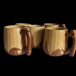 May include: Set of four brown and beige ceramic mugs with a corn cob design and bamboo handles.