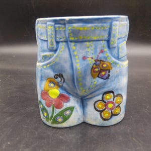 May include: A ceramic planter shaped like a pair of blue jeans with yellow stitching and colorful flower and butterfly designs.