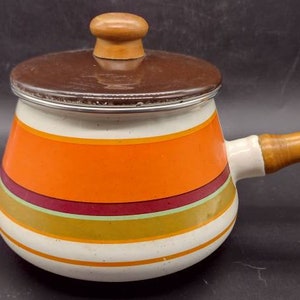 May include: A white enamel saucepan with a brown lid and wooden handle. The saucepan has orange, red, and green stripes around the body.