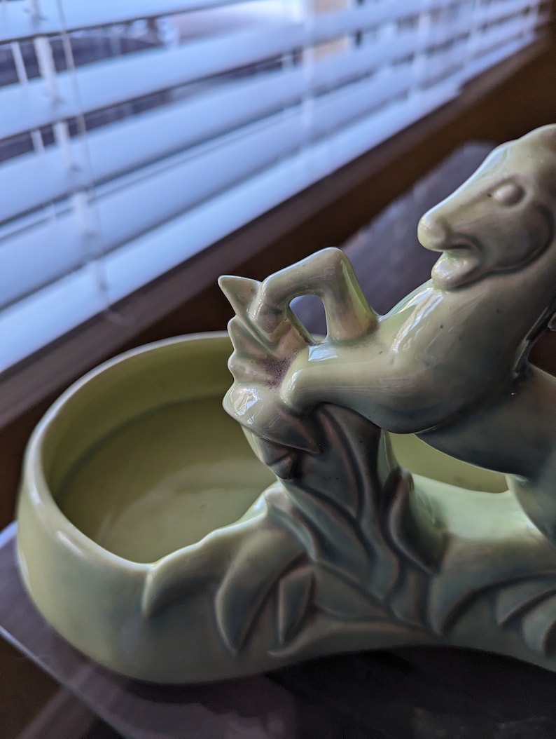 Pu&ograve; includere: Un vaso da fiori in ceramica verde a forma di cavallo con un design a foglie. Il vaso ha una parte superiore rotonda e aperta per la semina.