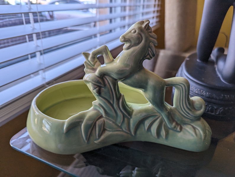 Pu&ograve; includere: Un vaso da fiori in ceramica verde a forma di cavallo con un design a foglie. Il vaso ha una ciotola poco profonda per contenere le piante.