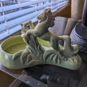 Pu&ograve; includere: Un vaso da fiori in ceramica verde a forma di cavallo con un design a foglie. Il vaso ha una ciotola poco profonda per contenere le piante.