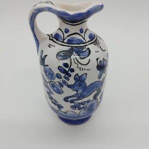 Peut inclure: Un petit pichet en céramique bleu et blanc avec un motif floral et animal. Le pichet a une anse et un corps arrondi.