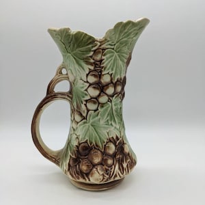 Könnte beinhalten: Eine Keramikvase mit einem braunen und grünen Traubenmuster. Die Vase hat einen Henkel und eine breite Öffnung.