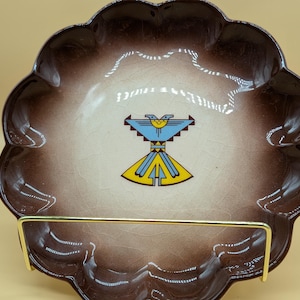 May include: A brown ceramic dish with a scalloped edge. The dish has a white center with a blue and yellow stylized bird design.