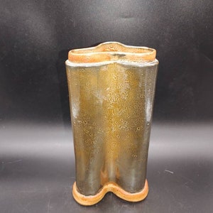 Puede incluir: Un jarrón de cerámica alto, hecho a mano, con una forma ondulada única. El jarrón presenta un esmalte verde oliva moteado con un borde y una base marrón anaranjado cálido. El diseño es moderno y orgánico.