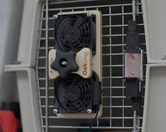 May include: A beige wooden fan attachment with two black fans and a black knob. The text "OakLines" is printed on the wood. The fan is attached to a metal cage.