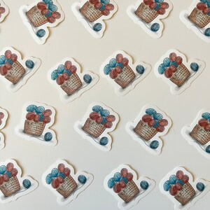 May include: A collection of 16 stickers featuring a basket overflowing with colorful yarn balls. The stickers are arranged in a grid pattern on a white background.