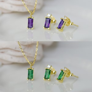 May include: A gold necklace and earrings set with a purple and green rectangular gemstone pendant and matching earrings.