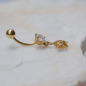 Può includere: Anello per ombelico dorato con un cristallo trasparente e un ciondolo a forma di stella.