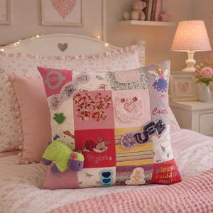 May include: A square patchwork throw pillow featuring various pink, white, and yellow fabric squares with embroidered designs, including a butterfly, a fairy, Piglet, and a small plush green and purple animal attached to the front surface.