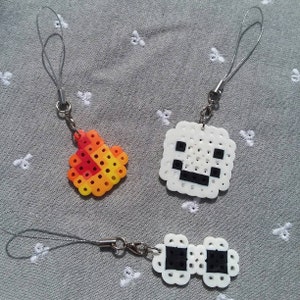 May include: Three white pixel art keychains with black details. One keychain is a square with a face, another is a flame, and the last is a pair of glasses.