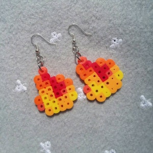 May include: A pair of dangle earrings with a heart-shaped design made of colorful plastic beads. The beads are arranged in a gradient pattern of red, orange, and yellow.