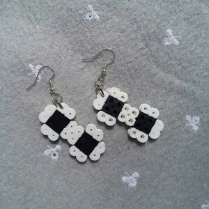 May include: A pair of black and white beaded earrings with silver hooks. The earrings are made of small, round beads that are arranged in a geometric pattern.