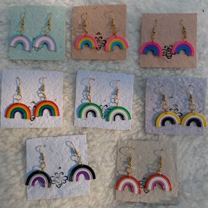 May include: Set of 10 rainbow-colored earrings with gold hooks. Each earring is a half-circle shape with different colored stripes. The earrings are displayed on small cards with a white background.