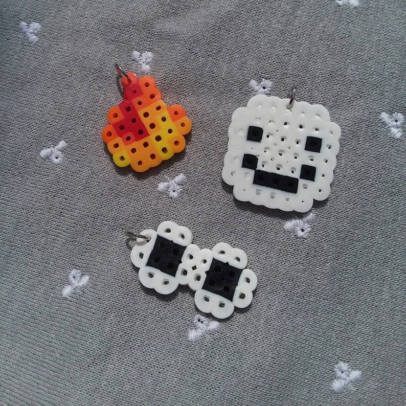 May include: Three pixel art keychains, each with a different design. The first is a red and yellow flame, the second is a white square with a black face, and the third is a white pair of glasses with black lenses.